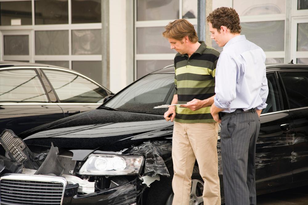A car crash lawyer explaining to a client what the average car accident settlement is worth in front of a damaged vehicle