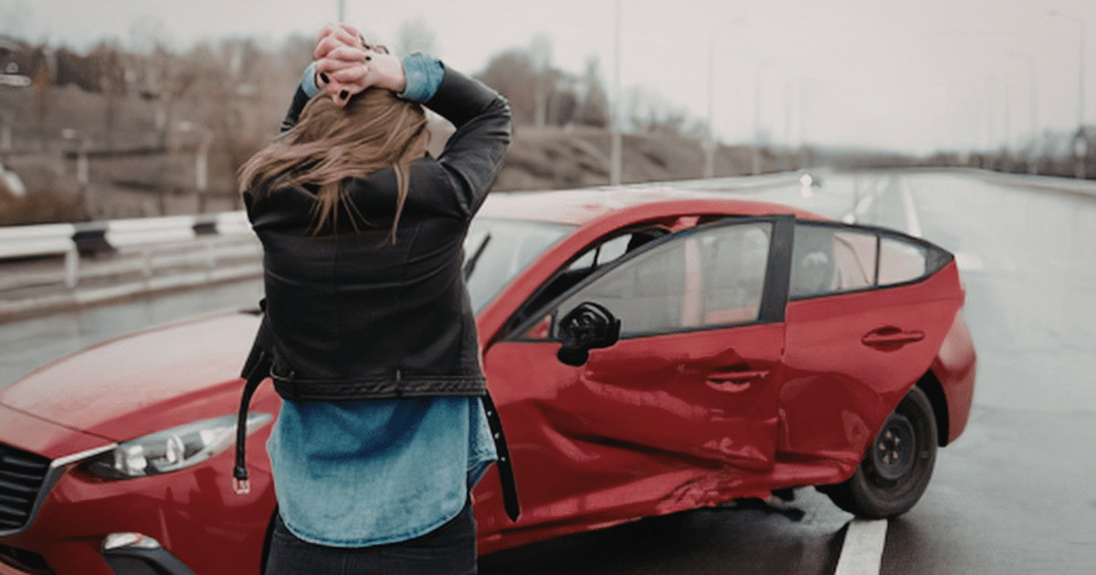 a distressed woman looks at her damaged car after an accident